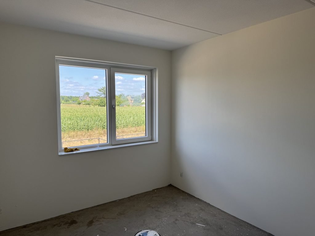 Lege kamer met gladde, lichte wanden, een betonvloer en uitzicht over een maisveld